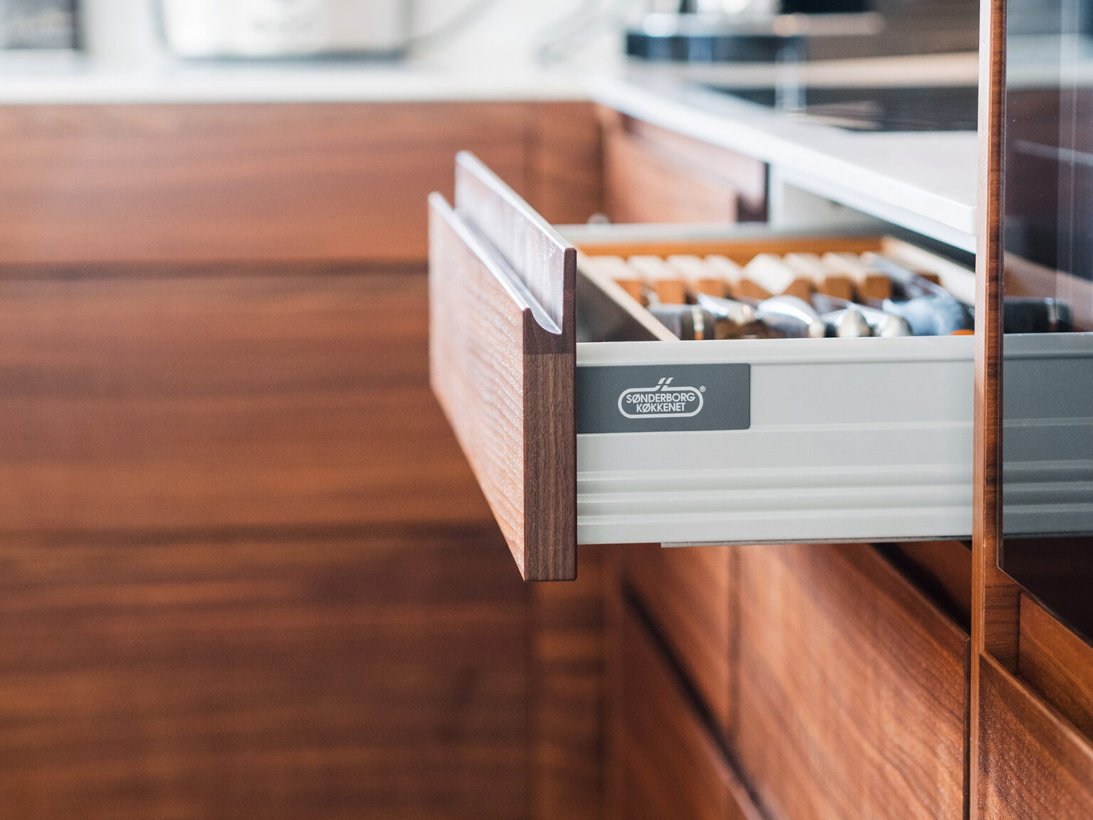 Køkken i valnød med varm, naturlig elegance og minimalistiske linjer, hvor materialernes kvalitet skaber et eksklusivt og roligt udtryk.